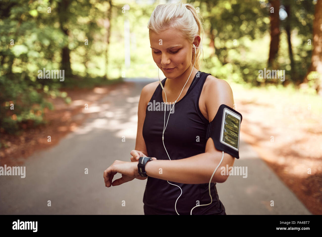 Fit young woman in sportswear son réglage montre de sport alors qu'il se trouvait sur un chemin forestier avant d'aller pour une course Banque D'Images