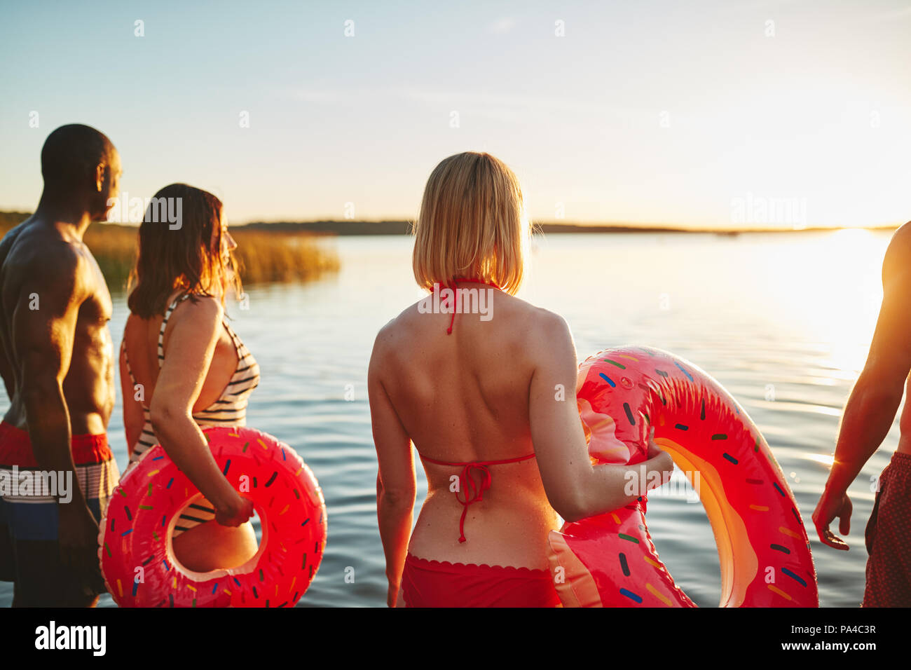 Coquille d'un groupe de jeunes amis diversifié en maillot de bain dans un lac permanent en regardant le coucher du soleil ensemble Banque D'Images