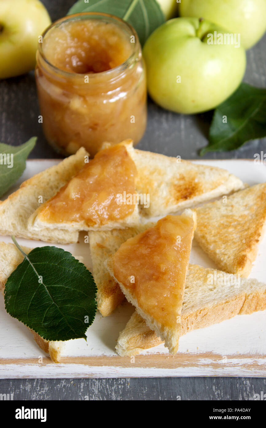 Confiture de pommes dans un bocal en verre avec du pain des tartines et des pommes mûres sur une surface en bois. De style rustique, selective focus. Banque D'Images