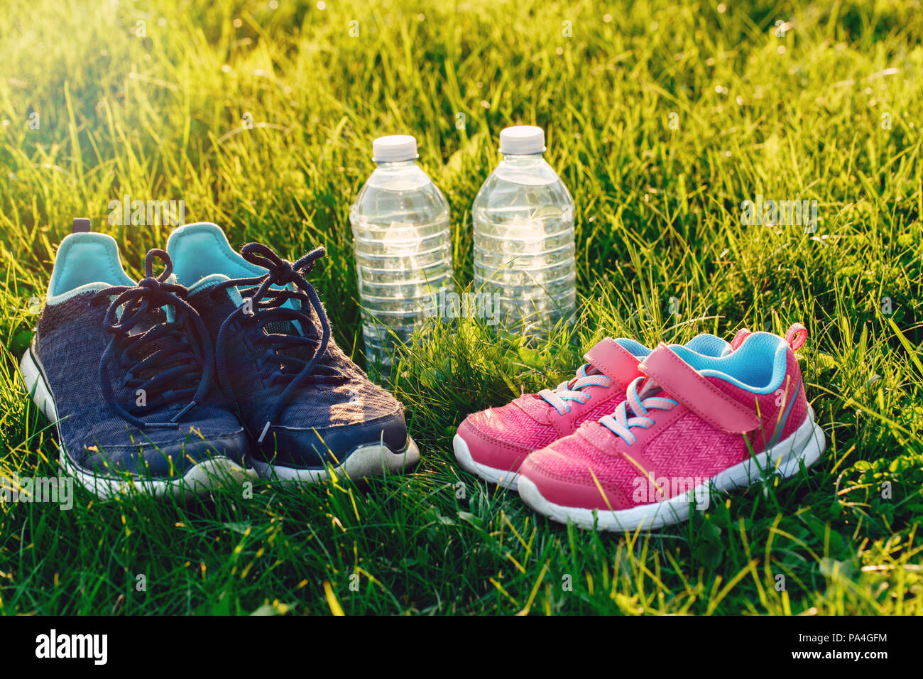 Macro gros plan de deux paires de chaussures et des bouteilles d'eau dans l' herbe verte à l'extérieur sur le coucher du soleil en soirée. Parents et  enfants adultes chaussures de sport ensemble.