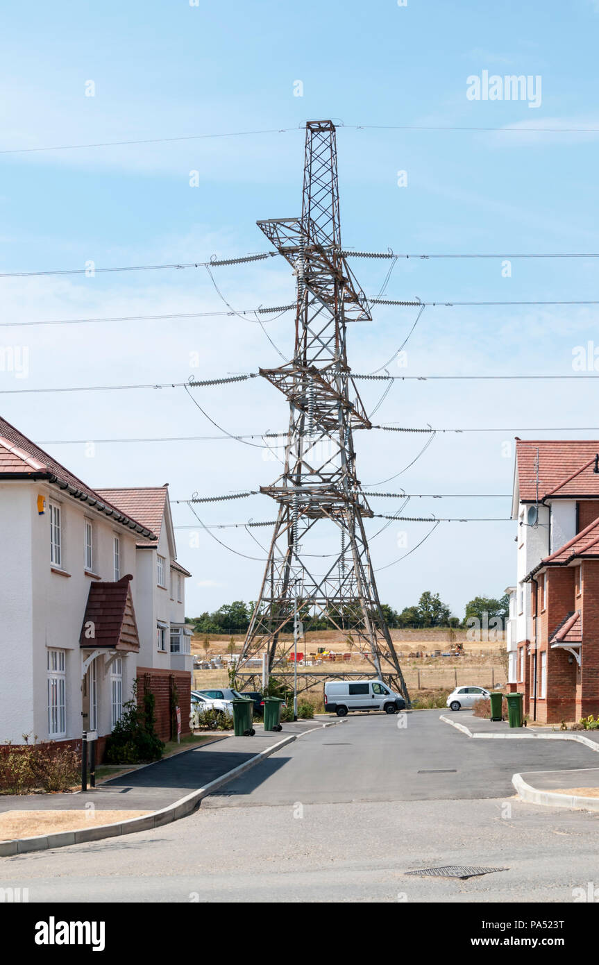 Une tour de transmission ou d'électricité pylône porte une ligne aérienne à travers une zone d'habitat à l'Ebbsfleet Garden City le développement. Banque D'Images
