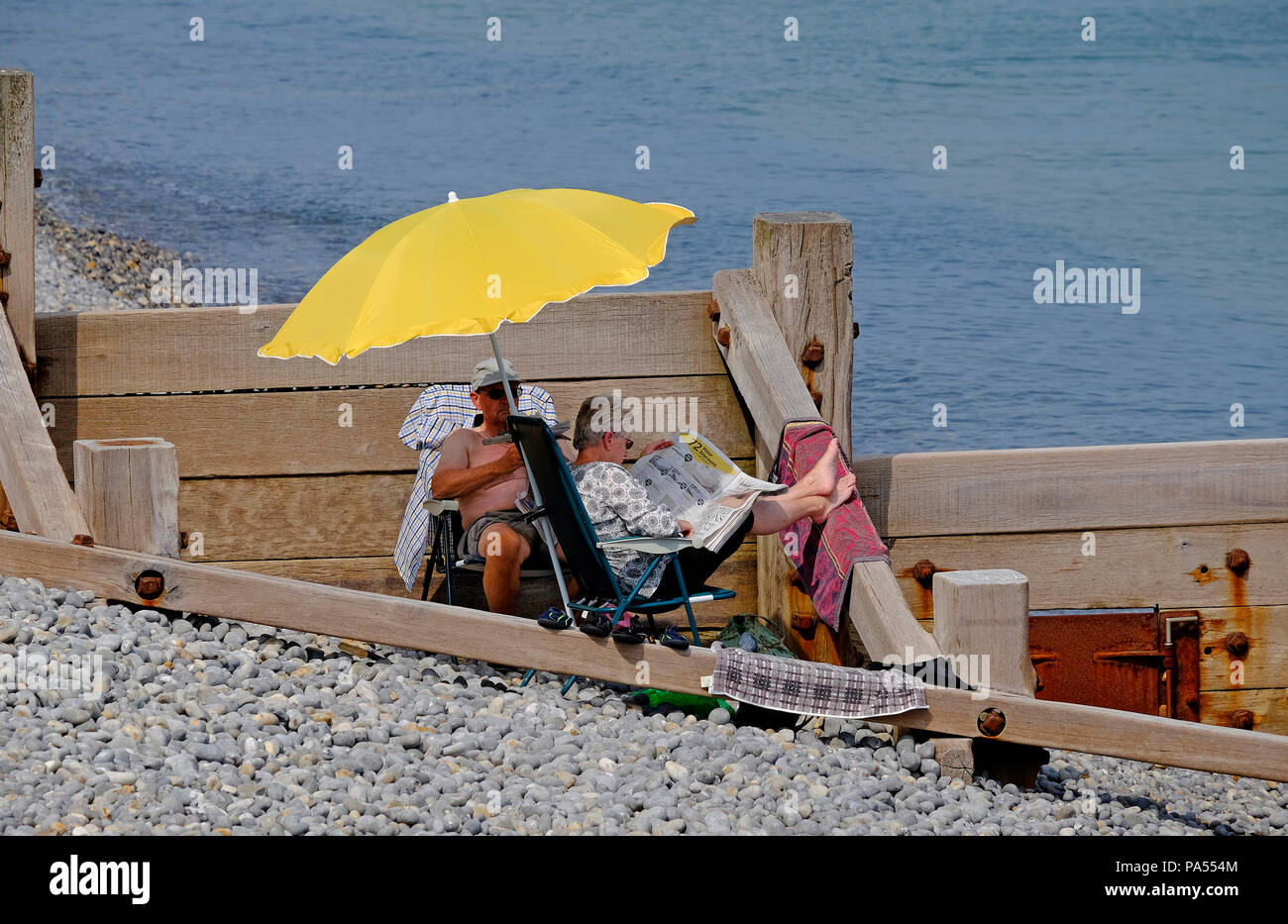 D'âge mûr assis sous un parasol jaune, sheringham, North Norfolk, Angleterre Banque D'Images
