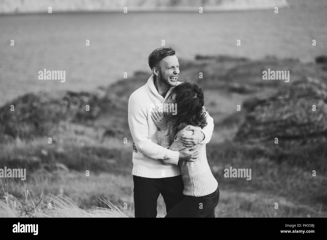 Jeune couple en train de marcher sur la côte de la mer nordique avec vue sur la montagne au printemps, les vêtements de style décontracté pulls et jeans. La tonalité noir et blanc Banque D'Images