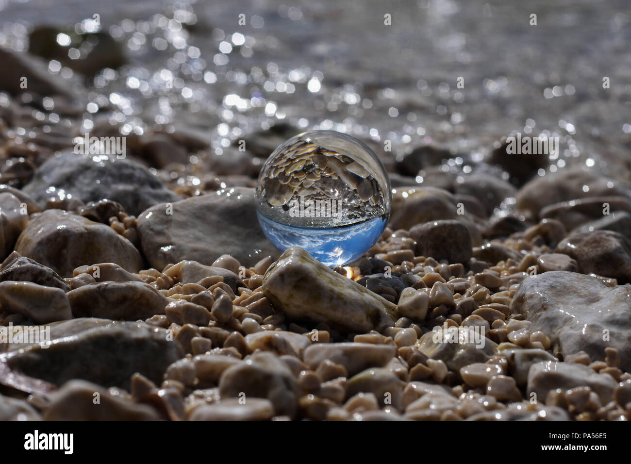 Bille de verre assis à Rocky beach whit mer vague se refléter dans ce/ conceptual image des vacances d'été Banque D'Images