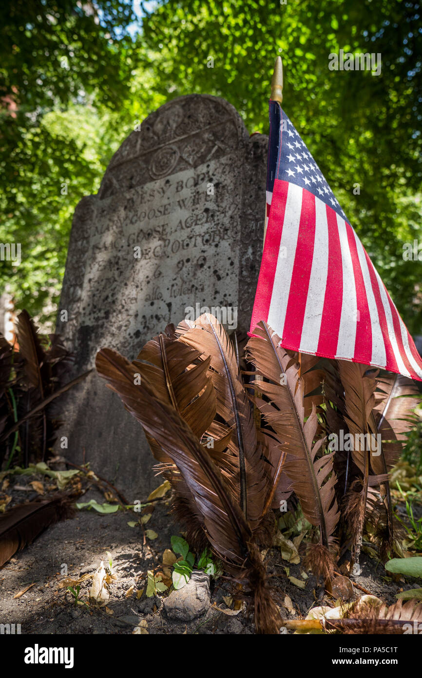 Close-up of mother oies pierre tombale avec brown des plumes d'oie et drapeau américain en premier plan, la dalle au milieu et vert feuilles en arrière-plan. Banque D'Images