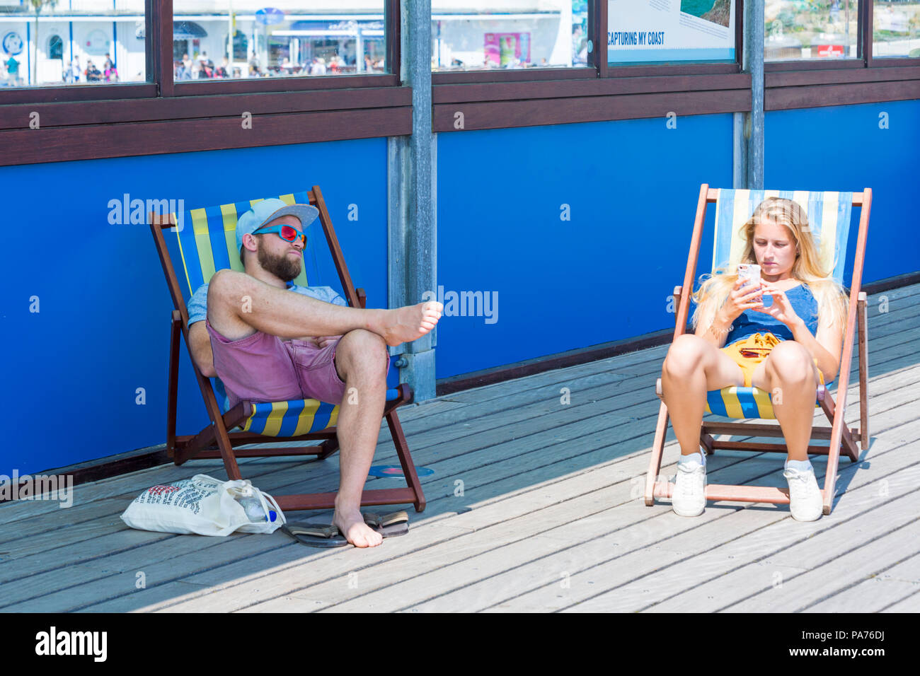 Bournemouth, Dorset, UK. 21 juillet 2018. UK : météo chaude et ensoleillée à Bournemouth plages, comme chef de la mer sunseekers pour profiter du soleil au début des vacances d'été. Dans l'ombre ou au soleil ? Couple de chaises longues sur la jetée de Bournemouth. Credit : Carolyn Jenkins/Alamy Live News Banque D'Images