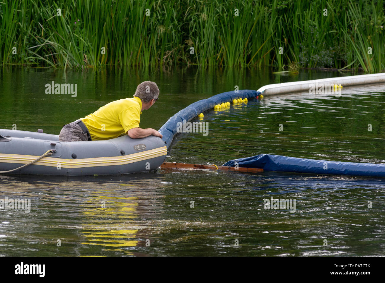 L'homme dans une chemise jaune dans un canot bateau sur une rivière gares de la ligne d'arrivée d'une course de canards en caoutchouc, partie d'un village anglais juste. Banque D'Images