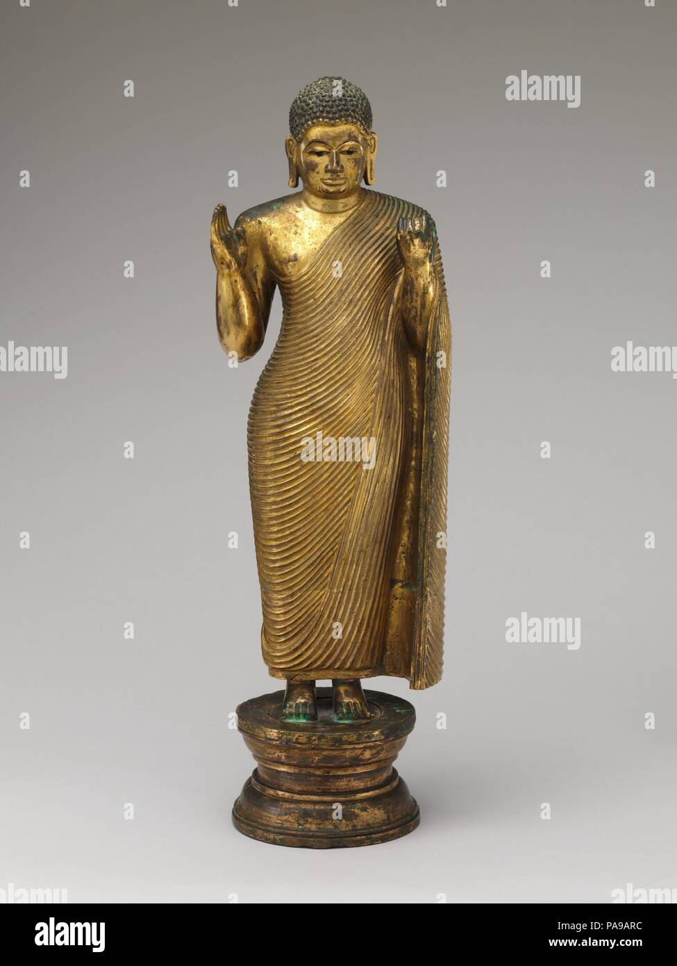 Offrant la protection de Bouddha. Culture : Sri Lanka. régions de l'ouest. Dimensions : H. 20 7/8 in. (53 cm) ; W. 5 7/8 in. (15 cm) ; Diam. du socle 5 7/16 in. (13,8 cm). Date : milieu du 15ème-16ème siècle. Cet imposant Bouddha rend l'Abhaya mudra geste avec sa main droite, en faisant preuve de compassion protection, tandis que sa main gauche prend en charge la grande chute de la robe monastique (uttarsanga). La monumentalité de l'icône est exceptionnel pour la période. Il fournit un pont stylistique entre un grand huitième siècle-fin-d'Anuradhapura style rock-cut Bouddha à Avukana et les chiffres corsé avec peignoirs dans styliz Banque D'Images