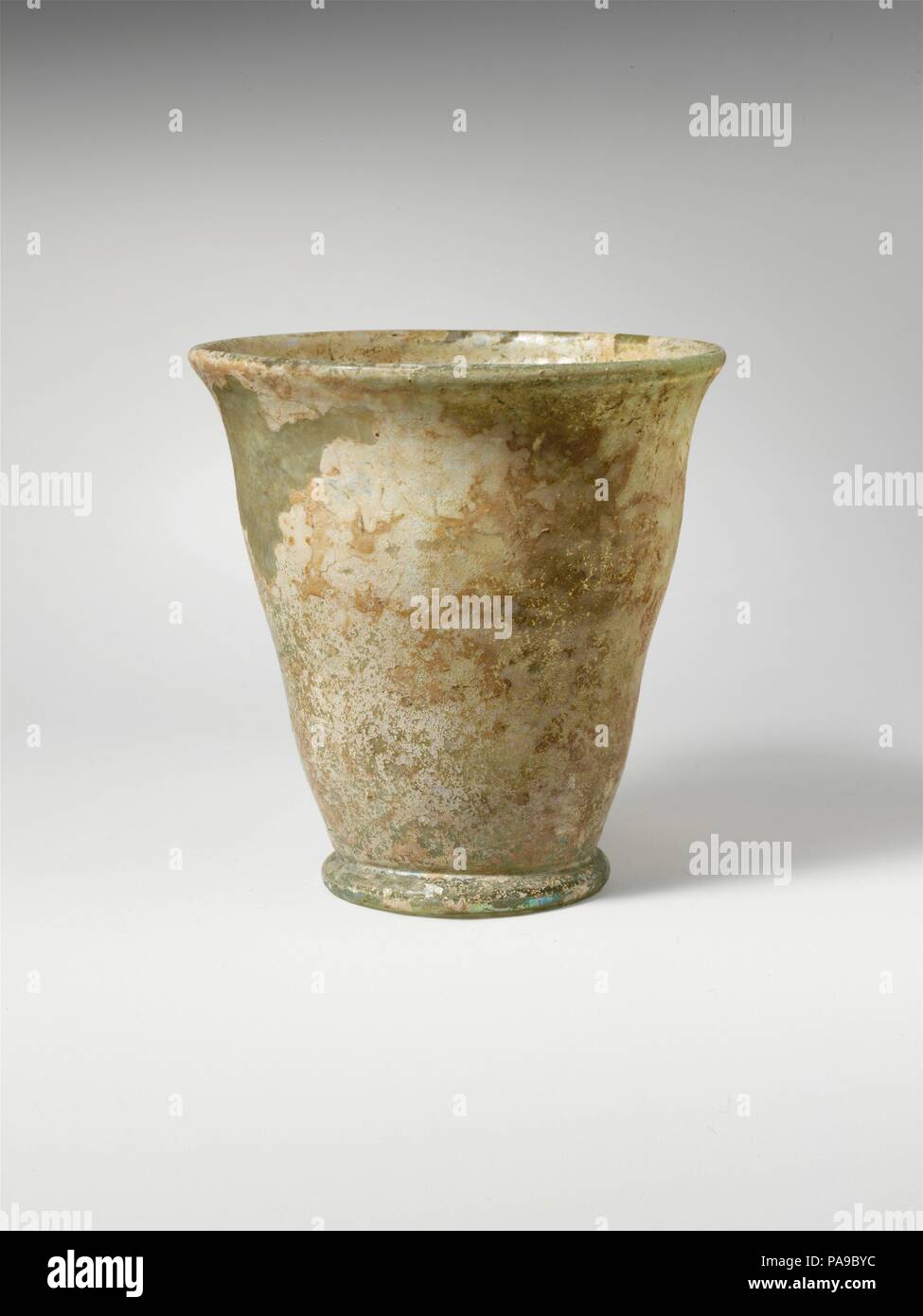 Bécher en verre. Culture : Roman. Dimensions : H. : 3 1/4 in. (8,3 cm). Date : 2ème-3ème siècle de notre ère. Bleu pâle translucide vert. Le torchage, épaissie, rim avec lèvre arrondie ; côté ondulant à corps, effilé à pied tubulaire plié ring ; faible, a souligné centre de kick à fond plat, avec grand circulaire pontil cicatrice. Intacts ; certains ternissement et iridescence mais la plupart des surfaces couvertes de l'altération à la crème. Musée : Metropolitan Museum of Art, New York, USA. Banque D'Images