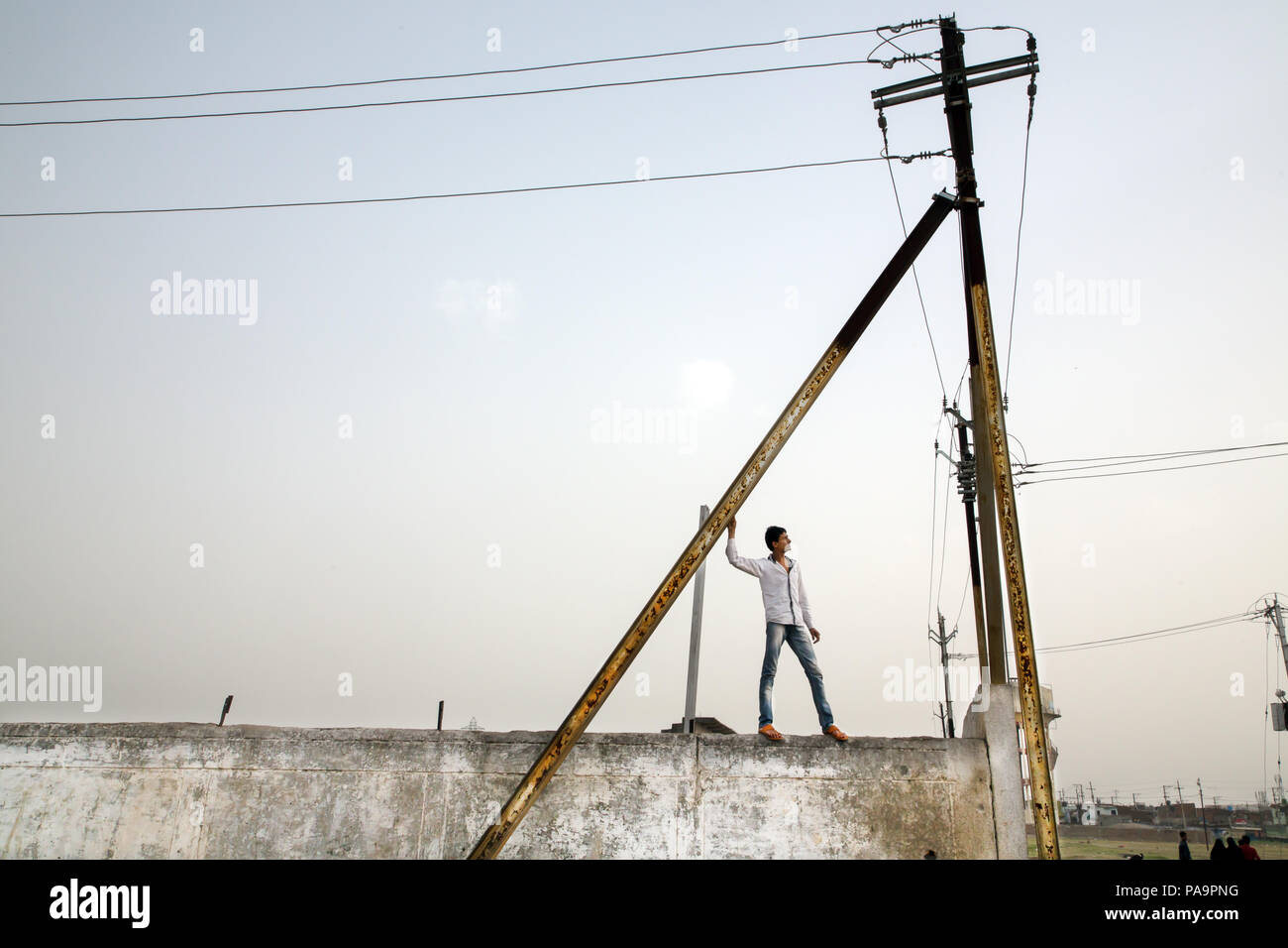 Un gars stans sur un mur près de pylônes électriques à Arif Nagar Colony. Bhopal, Inde Banque D'Images