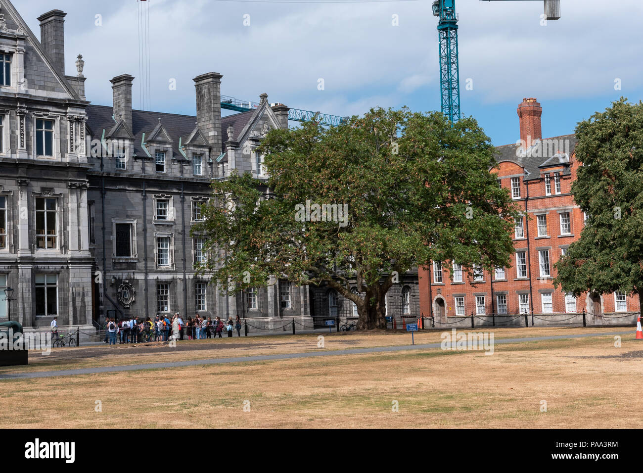 Un groupe touristique explore les motifs du Trinity College de Dublin, avec l'équipement de construction en arrière-plan. Banque D'Images