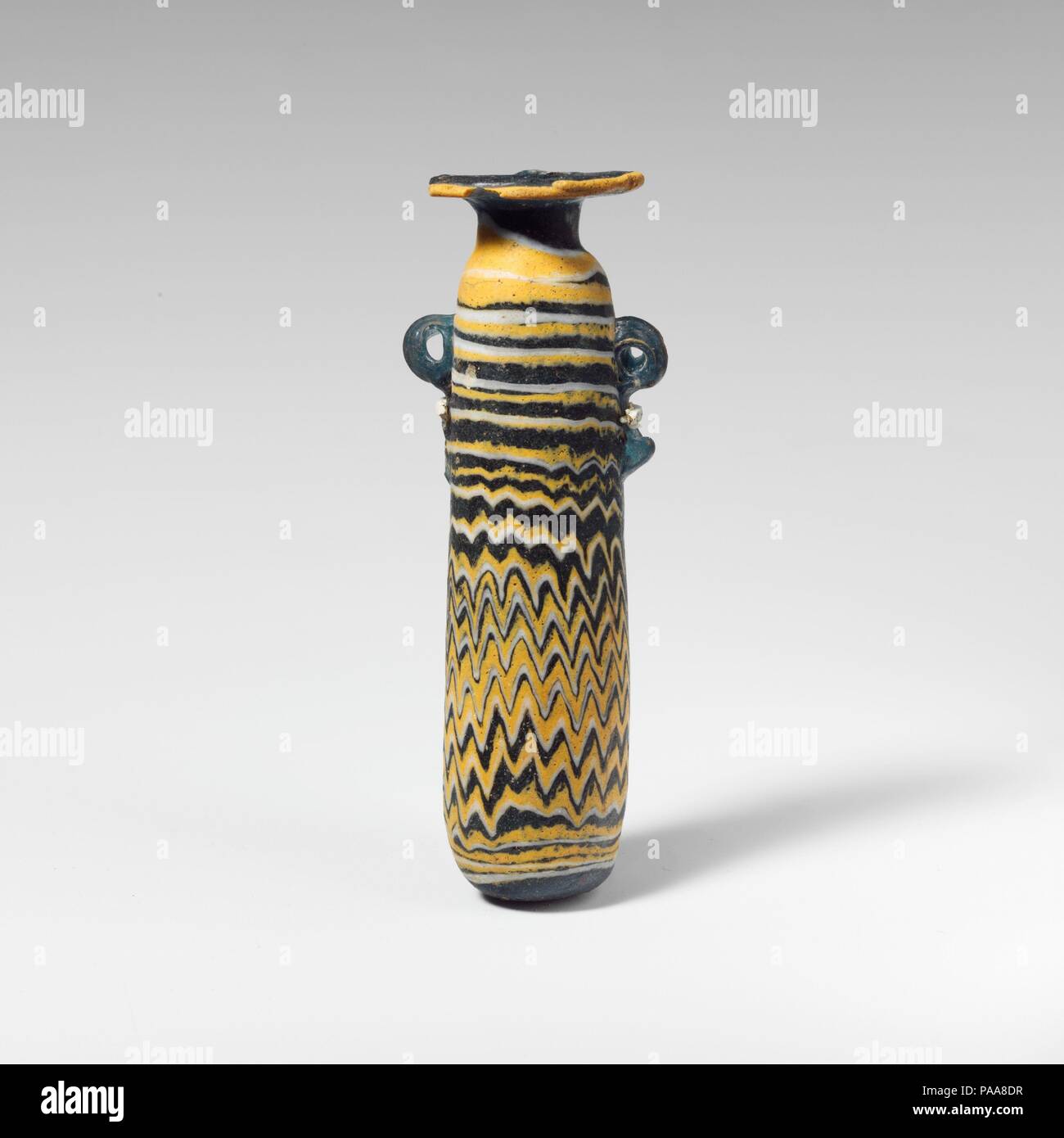 Alabastron en verre (flacon de parfum). Culture : le grec, l'Est de la Méditerranée. Dimensions : H. : 4 3/16 in. (10,6 cm). Date : 5ème siècle avant JC. Bleu clair translucide, avec poignées de même couleur ; sentiers en jaune opaque et blanc opaque. Horizontal large jante-disque, avec les marques des outils de rayonnement sur la surface supérieure du cou cylindrique court ; ; ; l'épaule arrondie corps cylindrique rectiligne conique convexe vers le haut avec ; bas ; deux poignées anneau vertical avec queues bulbés, appliquée sur la décoration du sentier. Itinéraire jaune attaché à bord de jante-disque ; une piste blanche recouverte avec du jaune autour du cou et inégalement plaie Banque D'Images