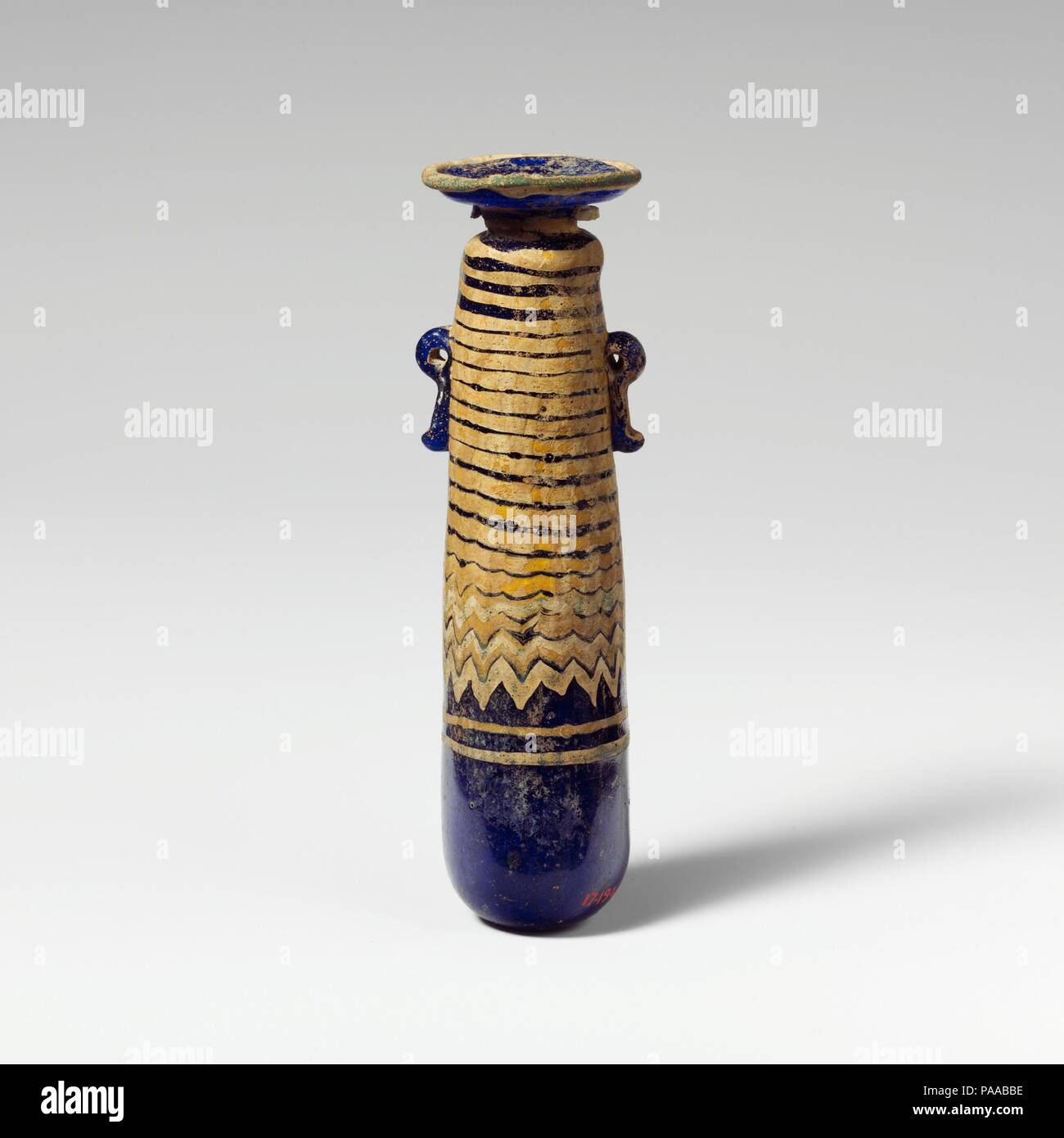 Alabastron en verre (flacon de parfum). Culture : le grec, l'Est de la Méditerranée. Dimensions : H. : 4 1/4 in. (10,8 cm). Date : fin 6ème-5ème siècle avant J.-C.. Bleu cobalt translucide, avec poignées de même couleur ; sentiers en jaune opaque opaque et bleu turquoise. Large, en pente vers l'intérieur du disque-rim, avec marques d'outils de rayonnement sur la surface supérieure et le bord irrégulier autour de la bouche, du cou cylindrique court vers le bas ; avec cône arrondi étroit ; l'épaule corps cylindrique rectiligne, effilé vers le haut ; bas convexe ; deux poignées anneau vertical avec queues bulbés, appliquée sur la décoration du sentier. Sentier bleu turquoise attaché à Banque D'Images