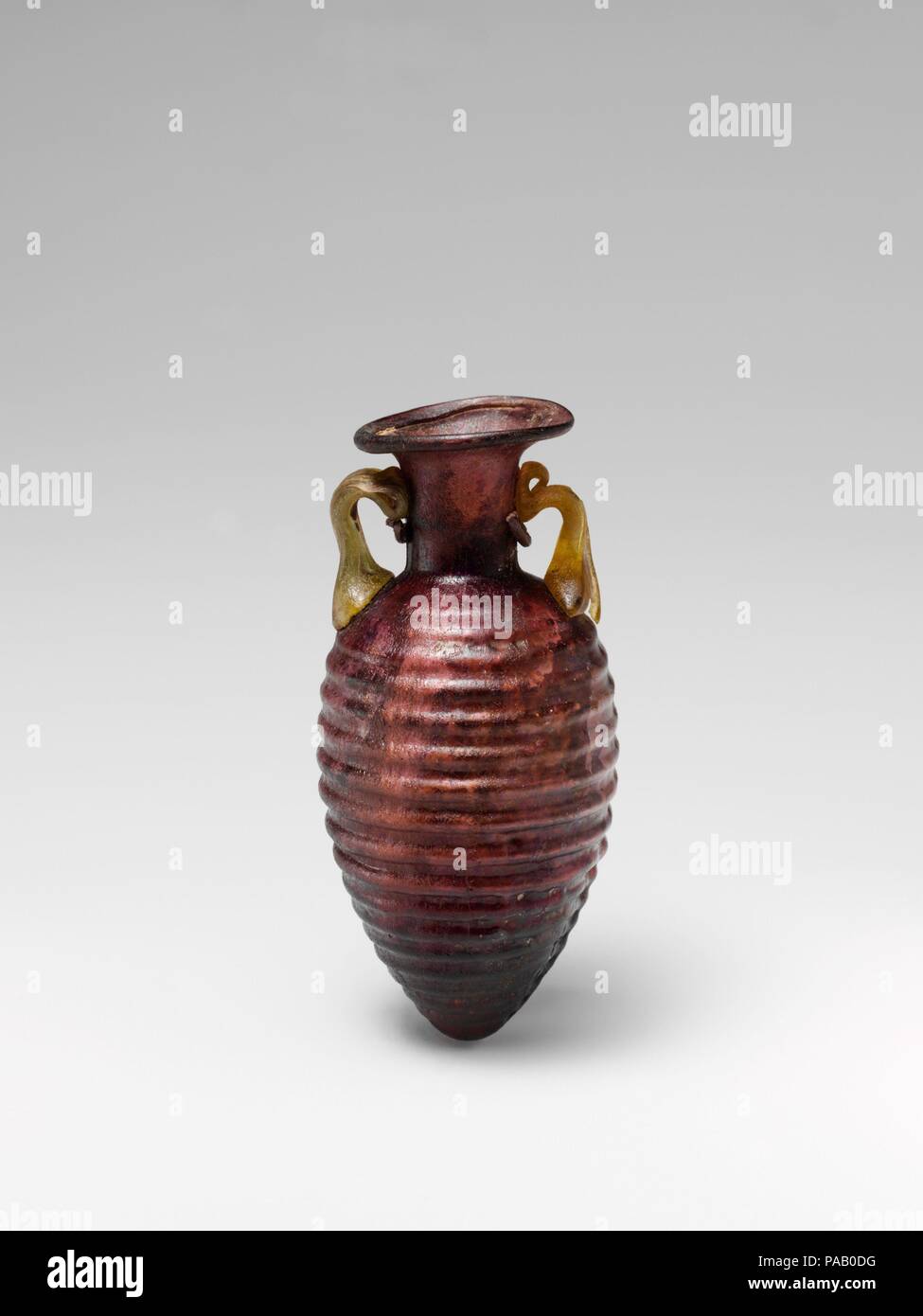 Amphoriskos en verre avec des nervures horizontales. Culture : Roman. Dimensions : H. 3 1/8 in. (7,9 cm) de diamètre 1 1/2 in. (3,8 cm). Date : 2ème moitié du 1er siècle de notre ère. Violet translucide ; poignées de pale jaune brunâtre. De plus, Rim, et dans, et transformées en bouche torchage, aslant à cou cylindrique, la moitié inférieure de ce qui est en retrait et porte les marques du moule en relief vertical au-dessous du haut des poignées ; corps ovoïde, effilé à fond pointu ; deux poignées avec deux nervures attaché au haut de caisse en pads, établis et sur côtés du cou, avec des pistes ci-dessus. Une seule couture moule autour de corps ; mol Banque D'Images