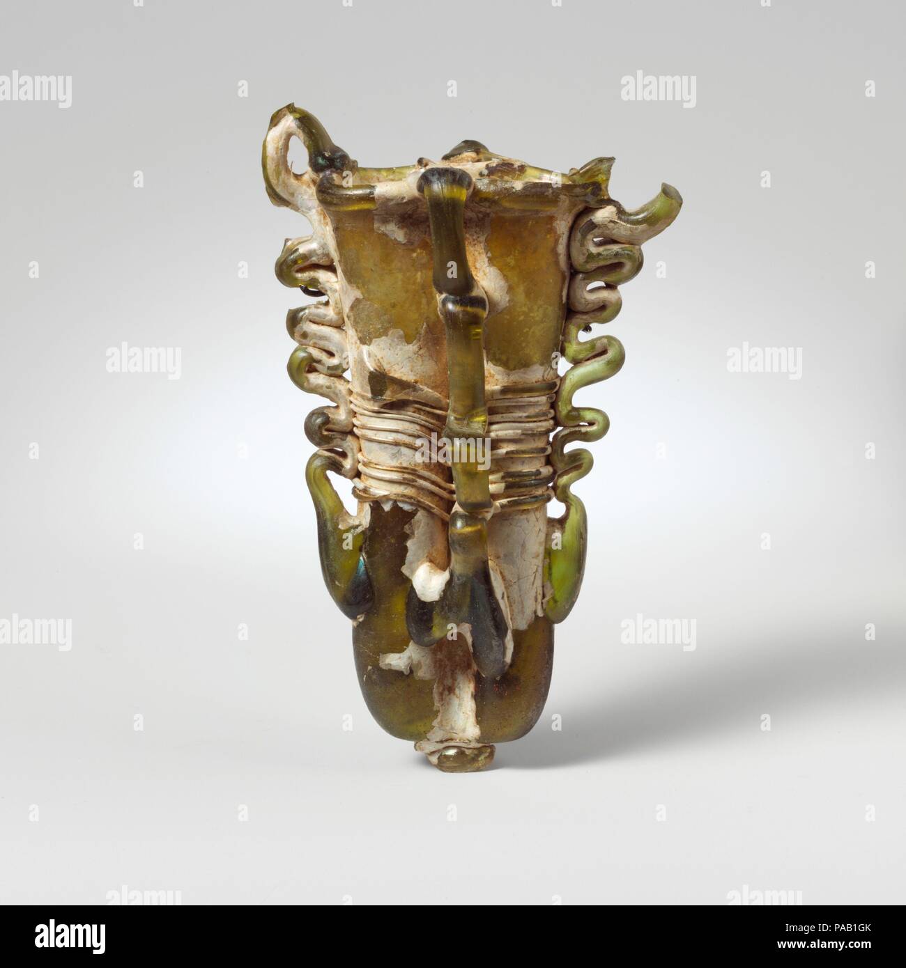 Double verre fiole cosmétique (kohl). Culture : Roman, république. Dimensions : hors tout : 4 13/16dans. (12.2cm). Date : 4ème siècle de notre ère. Jaune Vert translucide ; poignées et sentiers dans la même couleur. Jante tubulaire éversée, repliées et dans ; organe composé de deux tubes, côte à côte, faite à partir d'une seule collecte gonflés par le pincement d'autre verticalement pour faire grand, irrégulières ; diaphragme pontil application Notes de fond très épais ; deux poignées anneau attaché à la partie inférieure du corps en large, arrondie, tirées verticalement vers le haut et d'autre dans des boucles, puis se tourna vers le haut, vers le bas, et, formant des boucles au-dessus de la jante, et emmanché sur le bord supérieur de la jante Banque D'Images