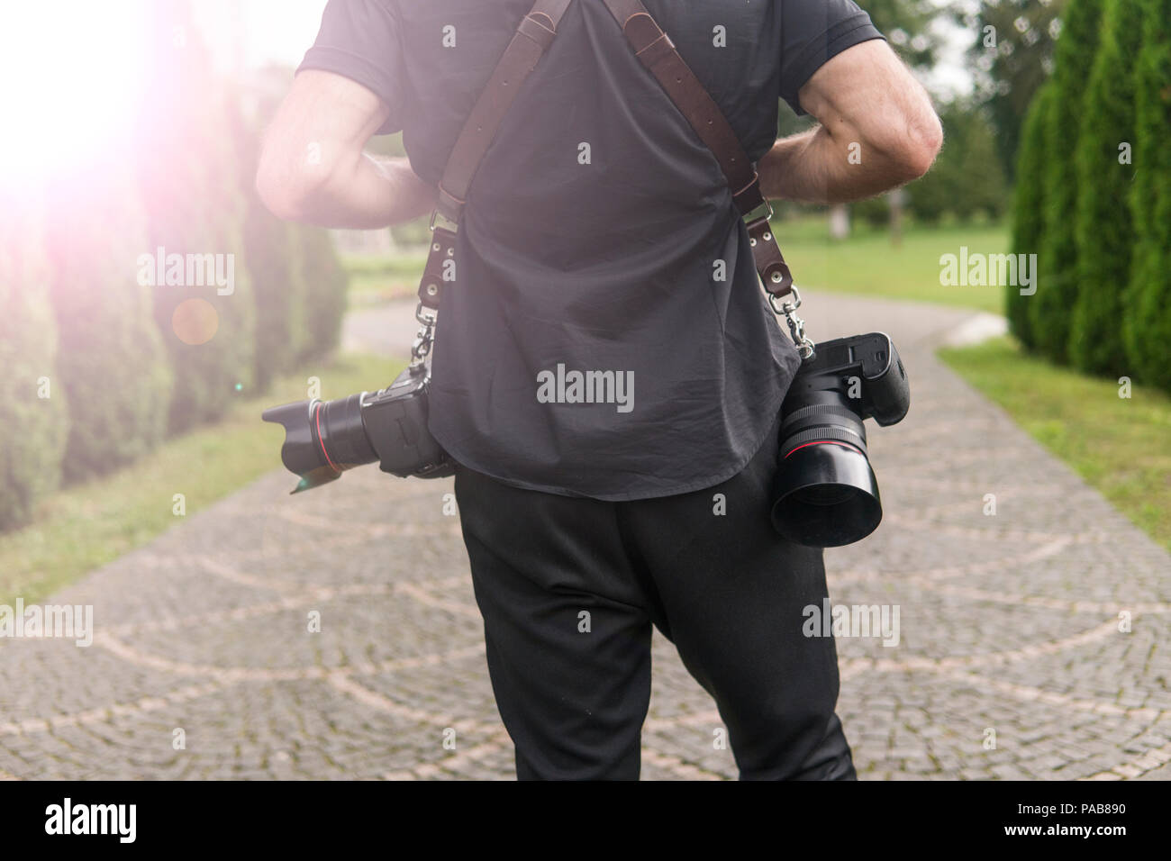 Retour de photographe de mariage professionnel en chemise noire et avec un deux caméras une bretelles un contre le jardin verdoyant. La photographie de mariage. Banque D'Images