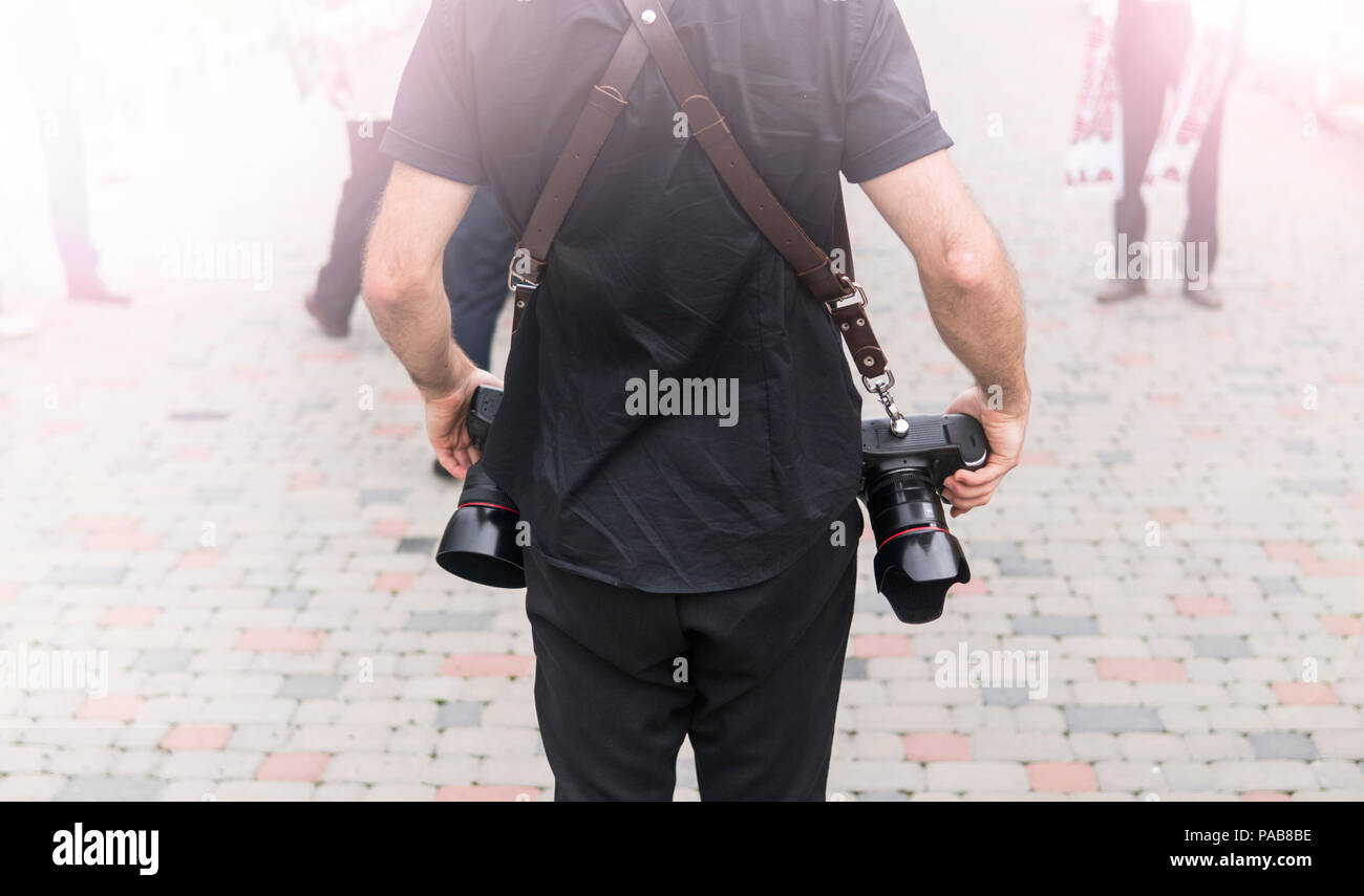 Retour de photographe de mariage professionnel en chemise noire et avec un deux caméras un a bretelles. La photographie de mariage. Banque D'Images