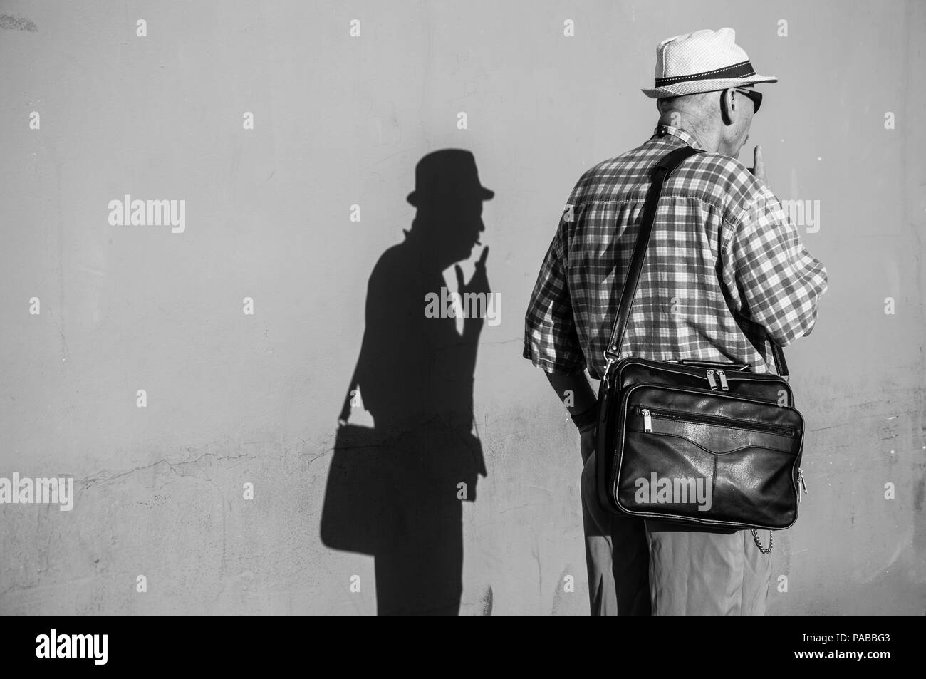 Un homme plus âgé par un mur permanent fumeurs et son ombre est sur le mur. Banque D'Images