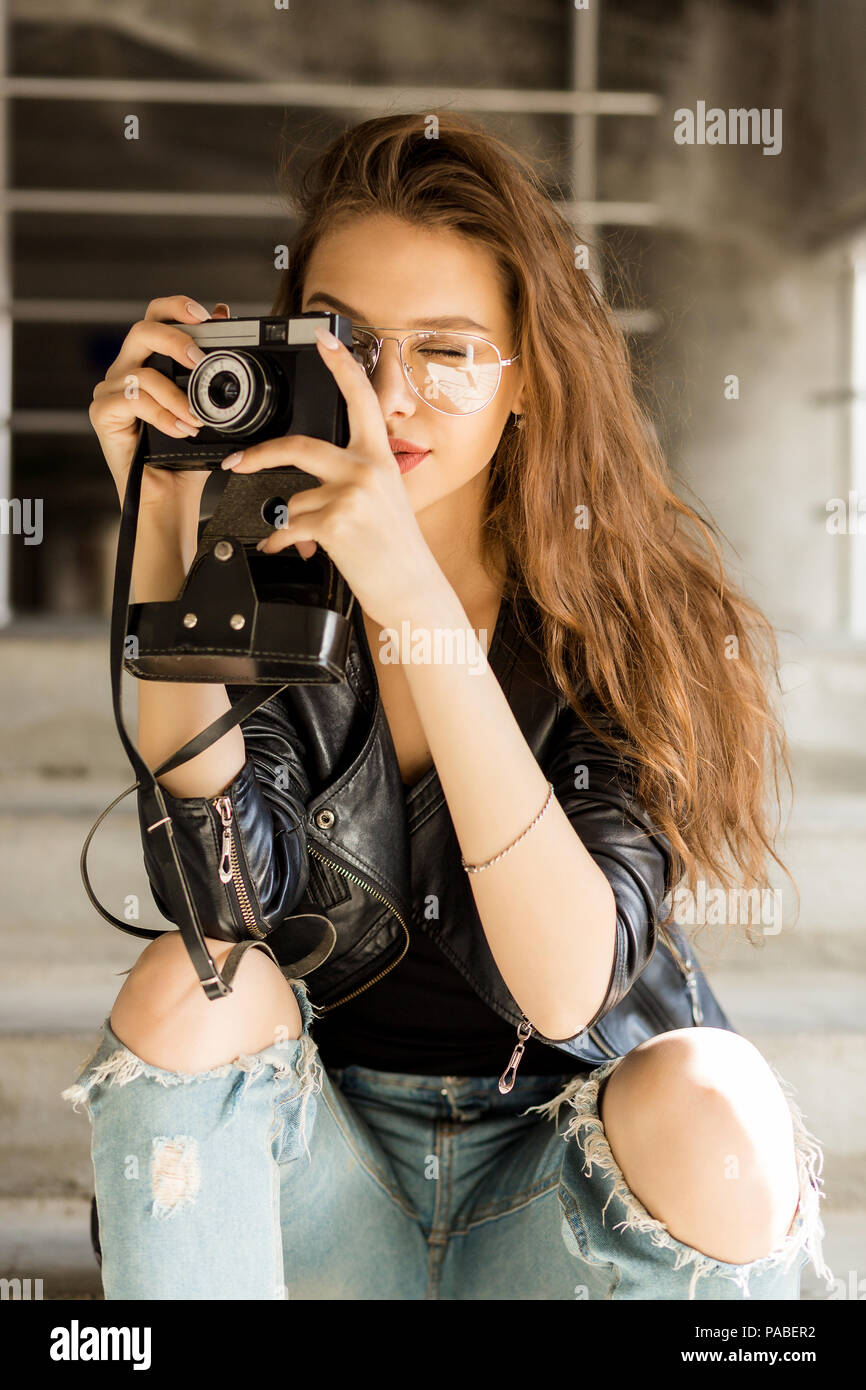 Photo de jeune femme gaie dans mode verres transparents portant une veste en cuir style rock black prendre photo sur vintage caméra. Ur Hipster Banque D'Images