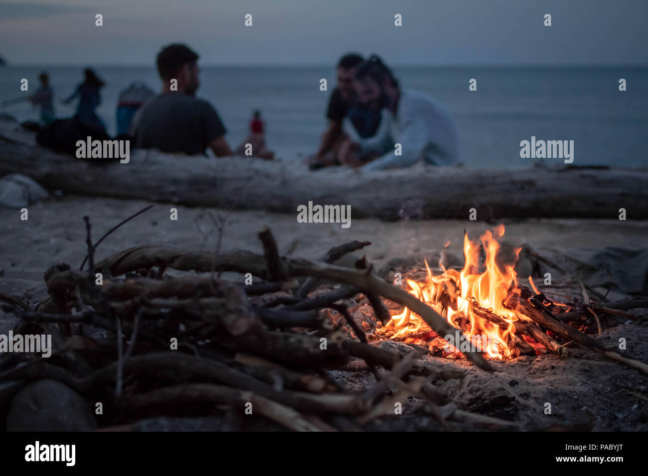 Feu de joie sur la plage par la mer au crépuscule avec un groupe d'amis dans l'arrière-plan Banque D'Images