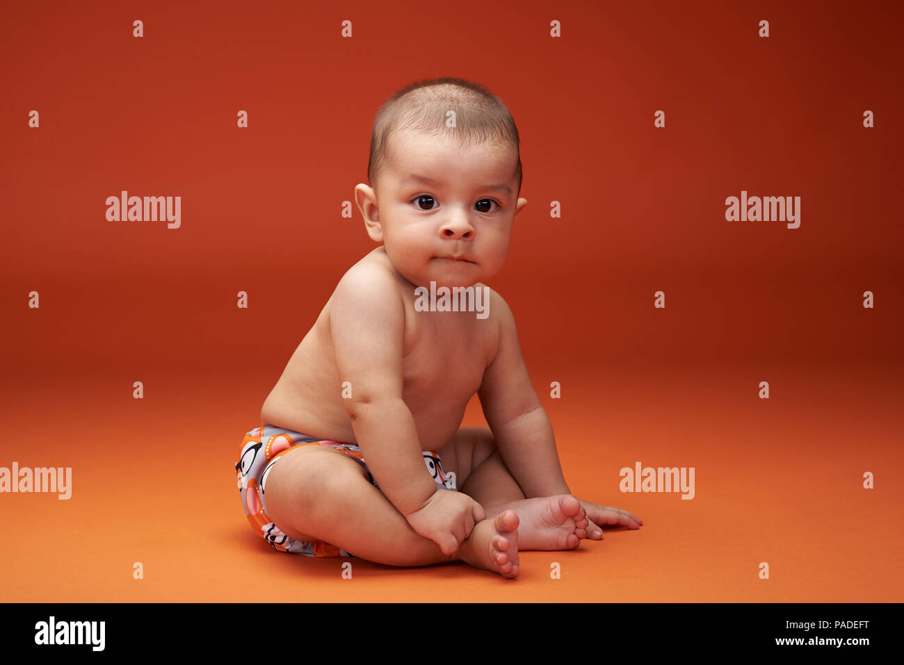 Un petit bébé garçon hispanique s'asseoir sur un fond de couleur orange Banque D'Images