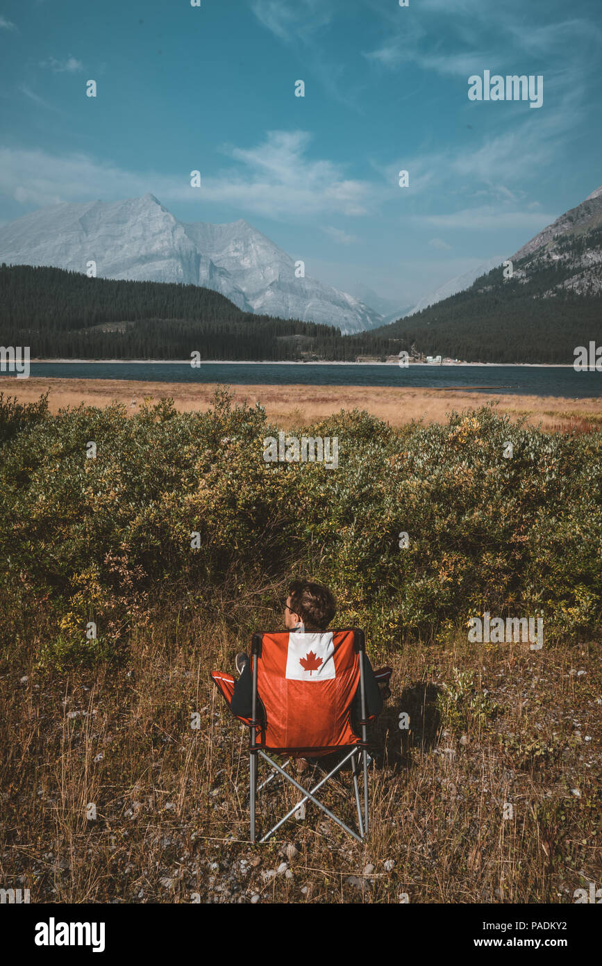 Chaises rouge vif avec logo canada donnant sur le lac et les montagnes avec de l'herbe en lac Lower Kananaskis, Canada Banque D'Images