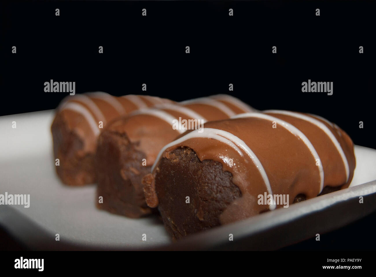 Trois gâteaux 'Kartoshka' se situent dans une ligne sur une plaque rectangulaire blanche. Sur un fond sombre Banque D'Images