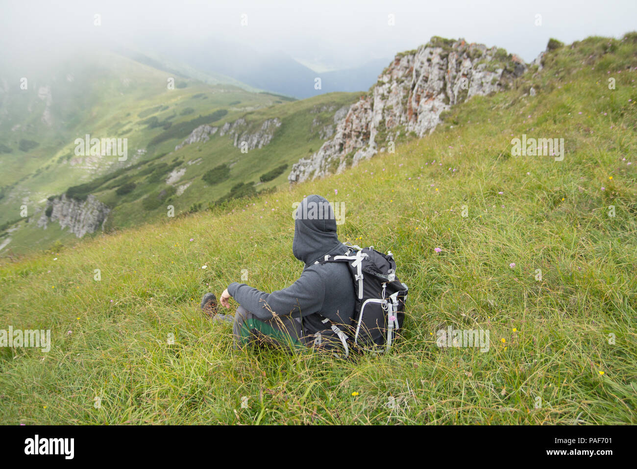 Vue arrière du sac à dos de randonneur assis sur l'herbe verte dans le paysage de montagne bénéficiant d'une vue panoramique Banque D'Images