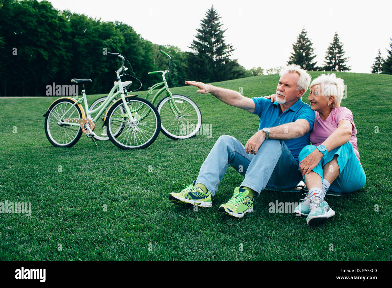 Vieux couple positif est assis sur l'herbe, avec leurs bicyclettes Banque D'Images