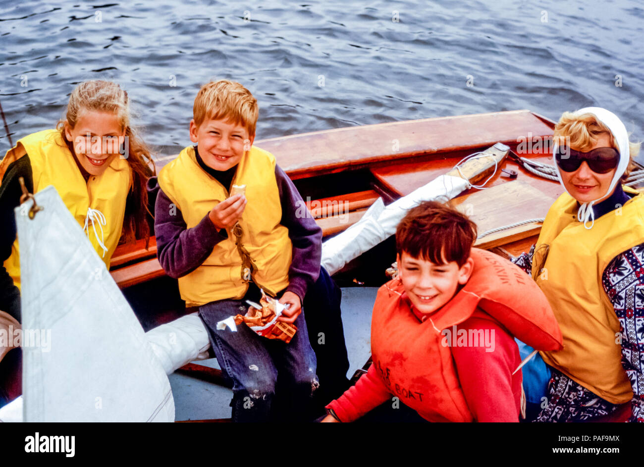 Famille d'une femme et de trois enfants portant un gilet de sauvetage dans  un petit bateau à voile sur la rivière Helford, en Cornouailles, en  Angleterre, au Royaume-Uni dans les années 1960