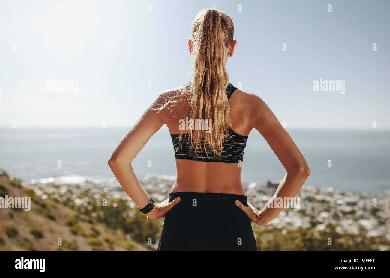 Vue arrière de la jeune femme debout avec ses mains sur les hanches et à la recherche à une vue. Coureuse de prendre pause de l'exécution. Banque D'Images