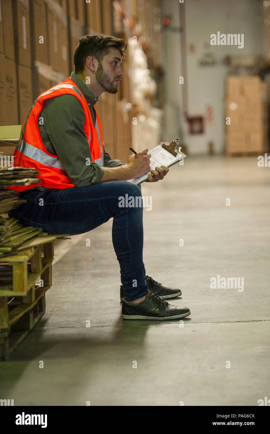 Worker writing on clipboard in warehouse Banque D'Images