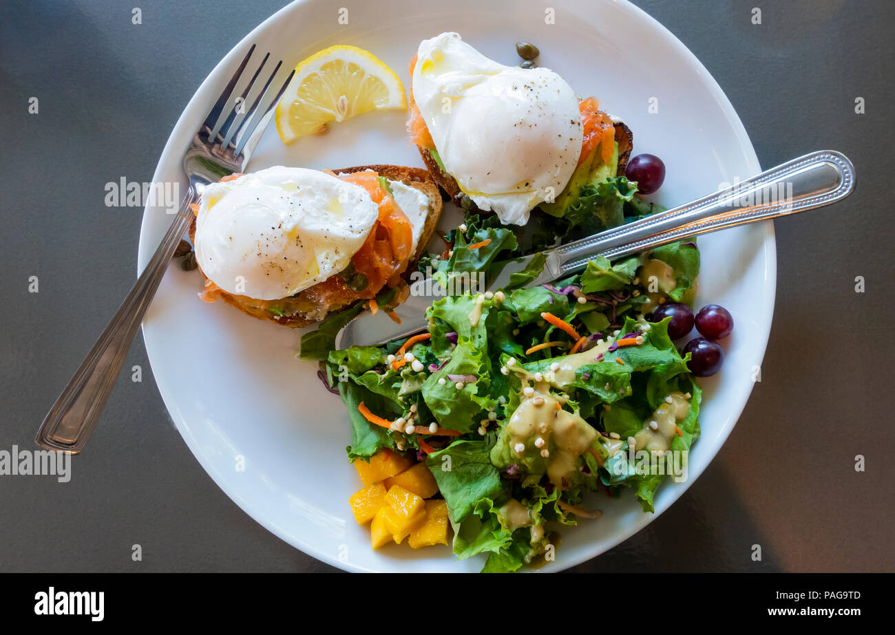 Deux œufs pochés avec saumon gravlax et avocat sur pain grillé de blé entier avec une salade verte mélangée avec des fruits dans un bistro à Montréal Banque D'Images
