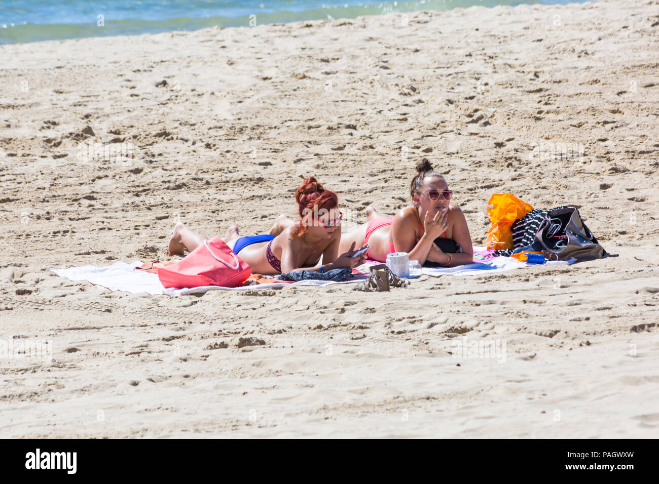 Bournemouth, Dorset, UK. 23 juillet 2018. Météo France : la canicule se poursuit à la hausse des températures sur une brulante et journée ensoleillée à plages de Bournemouth avec ciel bleu et soleil ininterrompue. La station de tête Sunseekers pour prendre le soleil. Deux femmes en train de bronzer sur une plage de fumer des cigarettes, on looking at mobile phone. Credit : Carolyn Jenkins/Alamy Live News Banque D'Images