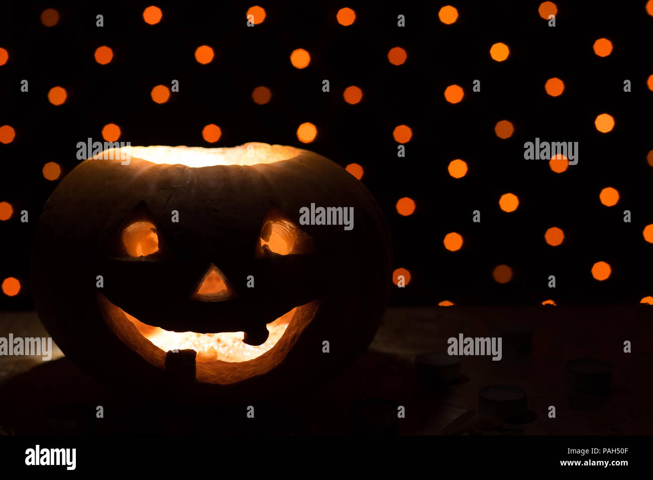 Orange citrouille comme une tête avec les yeux sculptés et un sourire avec des bougies allumées sur un fond noir avec une guirlande de la Halloween party Banque D'Images