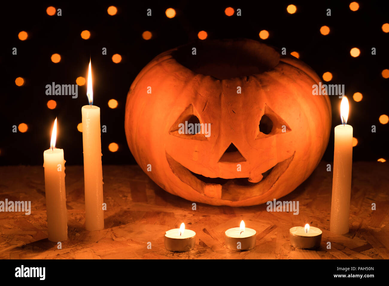 Orange citrouille comme une tête avec les yeux sculptés et un sourire avec des bougies allumées sur un fond noir avec une guirlande de la Halloween party Banque D'Images