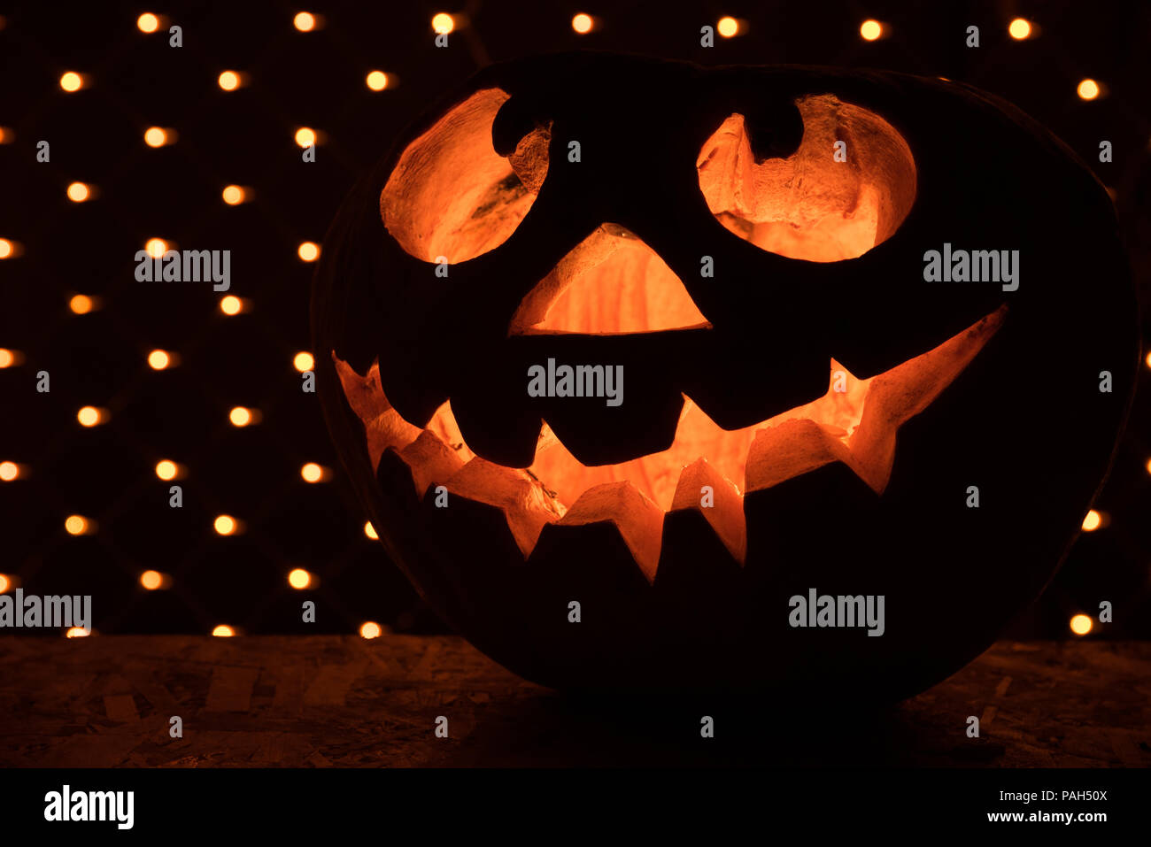 Orange citrouille drôle comme une tête avec les yeux sculptés et un sourire sur un fond noir avec une guirlande pour l'Halloween party Banque D'Images