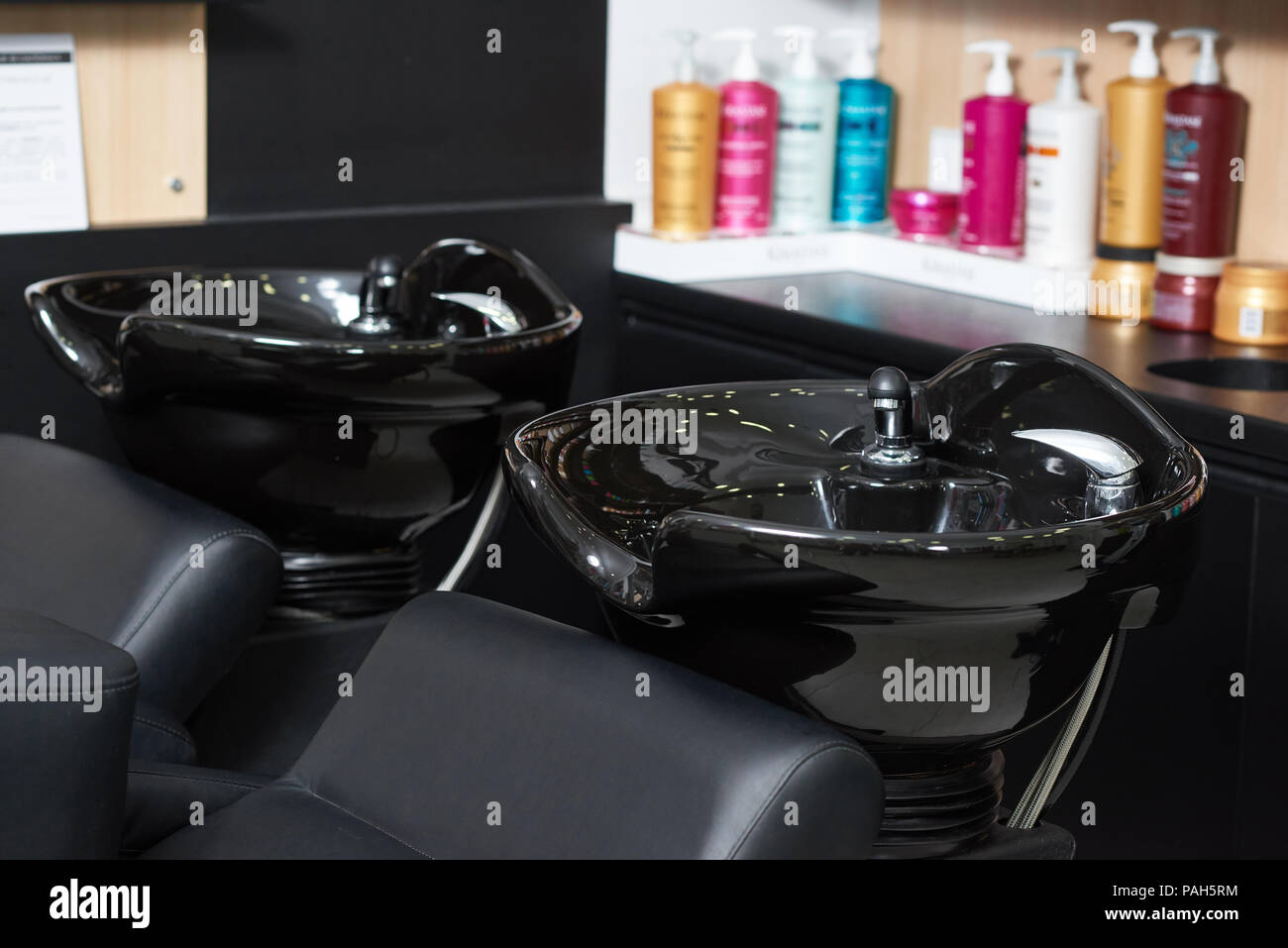 Photo de deux puits de cheveux noir ceramical standing in beaty salon avec produits haircair sur arrière-plan. Les bouteilles de plastique en couleur de cheveux pour la santé. L'intérieur moderne fait dans des couleurs sombres. Banque D'Images