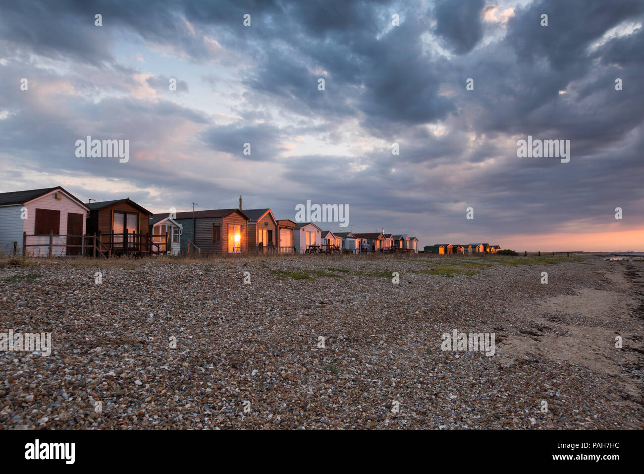 Golden sunset lumière brillant sur le cabanes de plage par la plage de galets à Seasalter, Whitstable, Kent, UK. Nuages spectaculaires sont vus ci-dessus. Banque D'Images