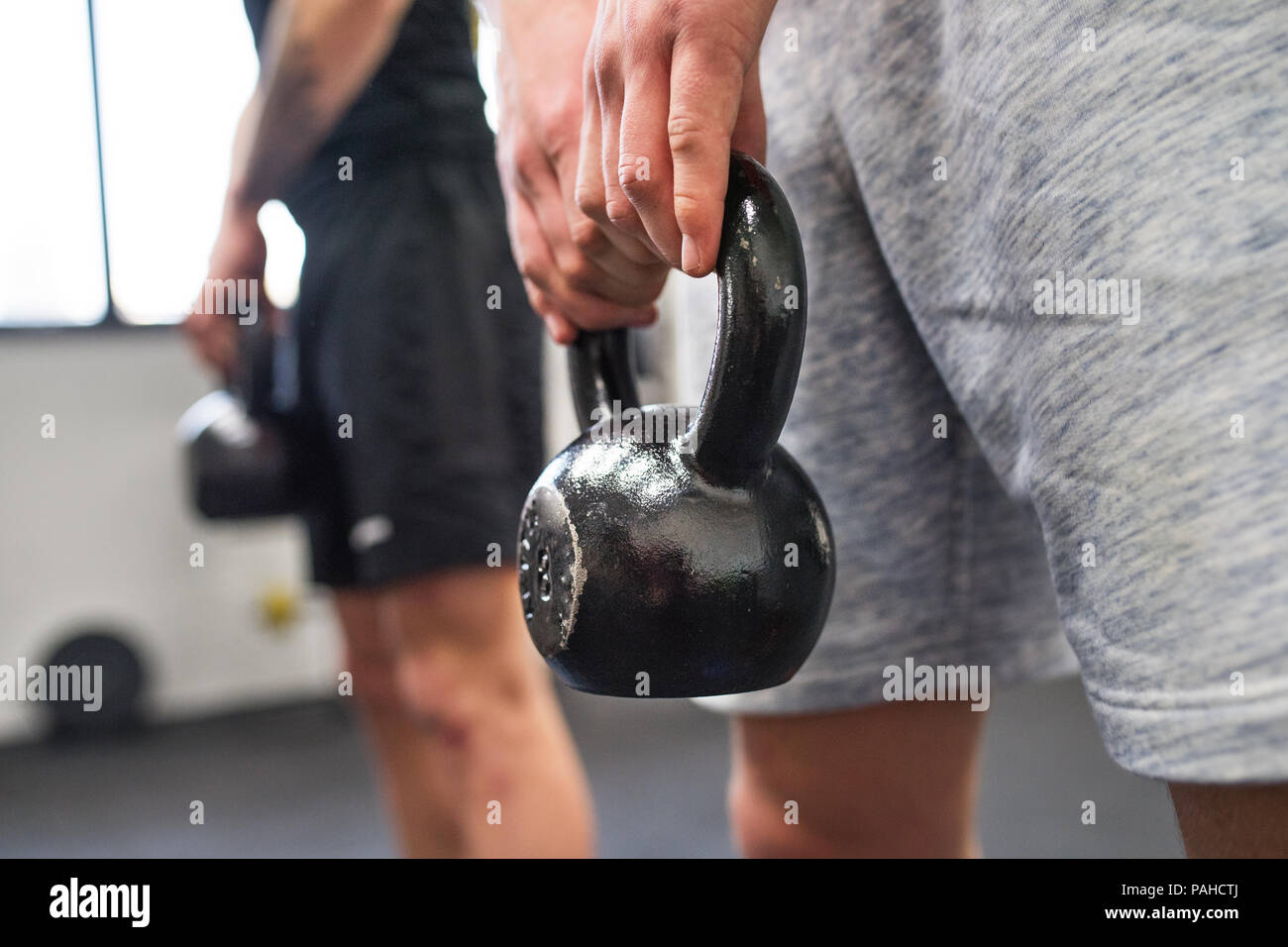 Méconnaissable de jeunes hommes dans une salle de sport faire kettlebell swings. Banque D'Images