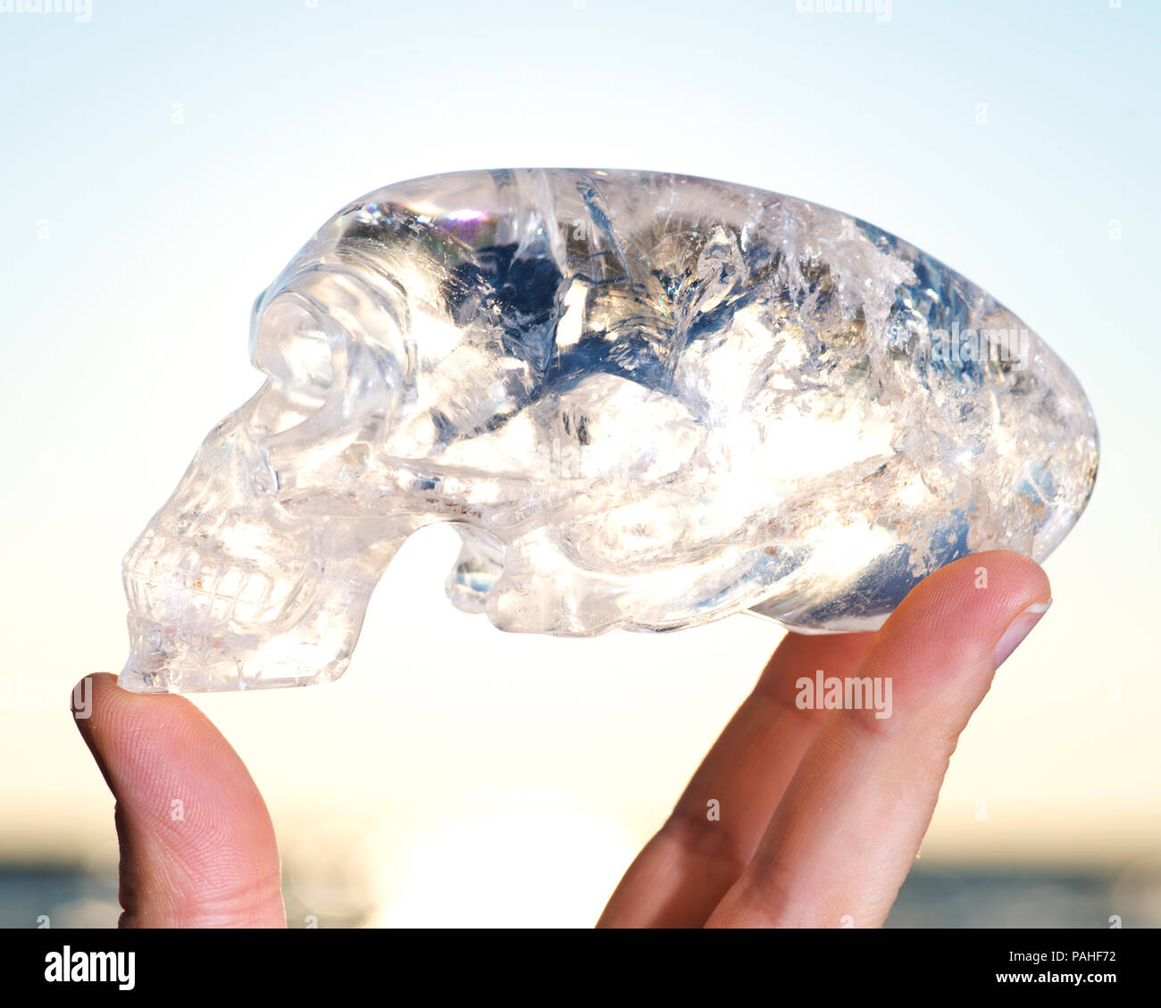 Woman's hand holding Maya allongé sculpté Quartz Crystal Skull exotiques au lever du soleil en face du lac. Banque D'Images