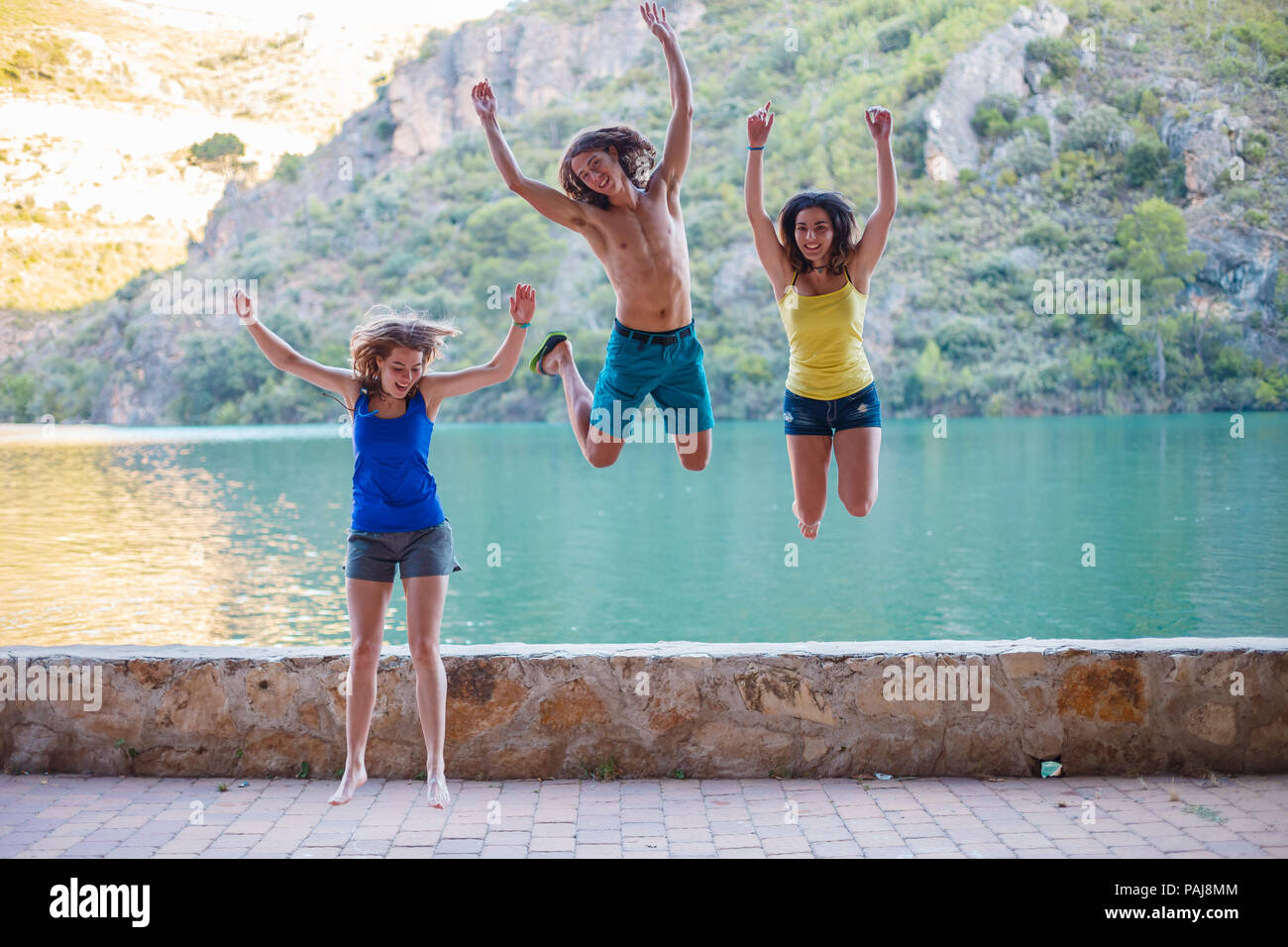 Les amis de sauter sur un remblai sur un lac turquoise dans les montagnes Banque D'Images