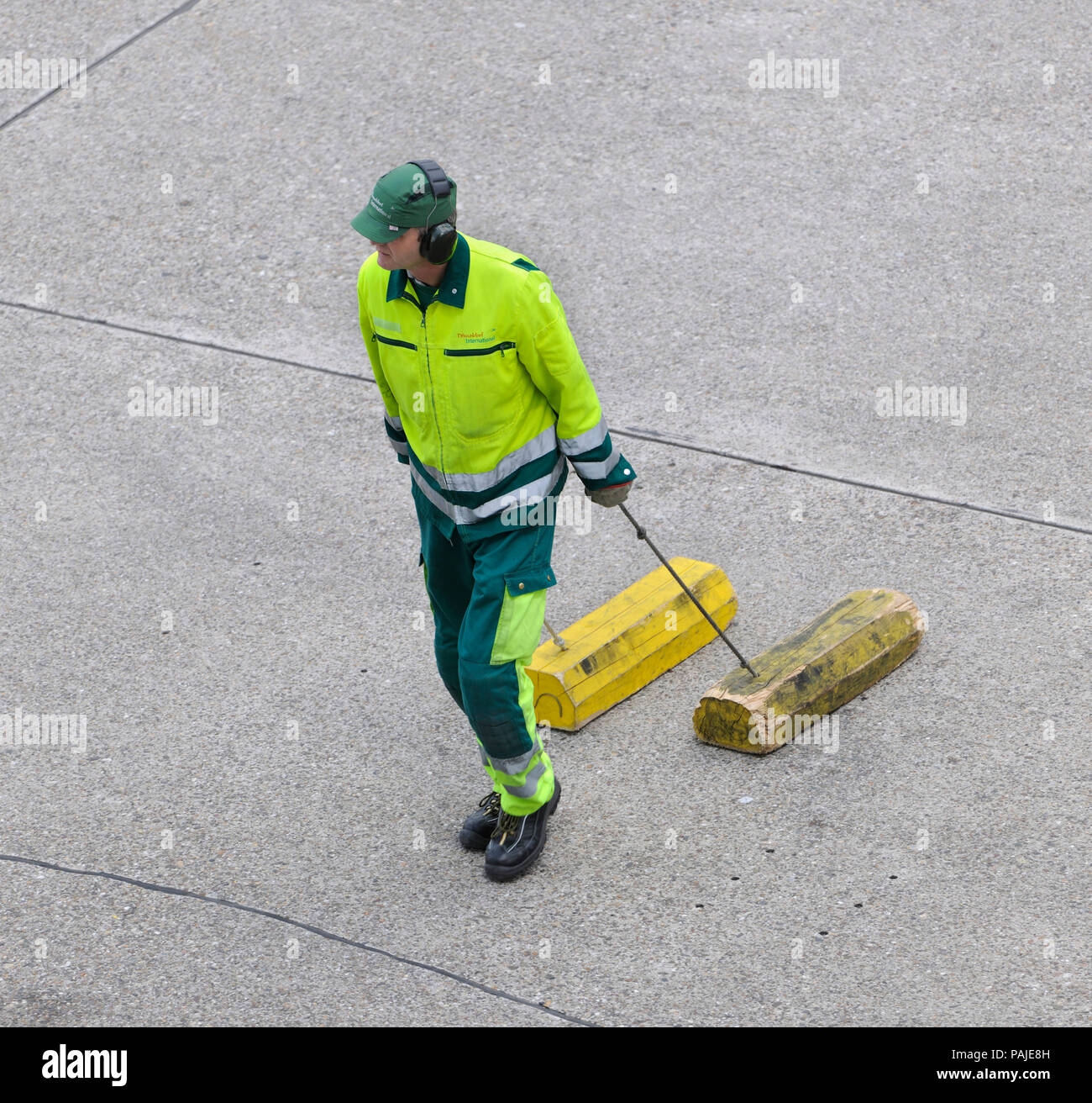 Homme portant une veste jaune-viz et ear-humains en faisant glisser des cales sur le tarmac Banque D'Images