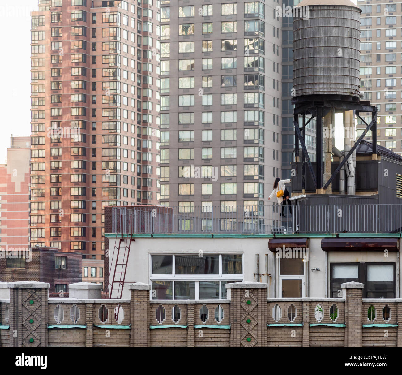 Bien habillé jeune femme monter à l'échelle d'un tour de l'eau sur le toit d'un immeuble de New York Banque D'Images