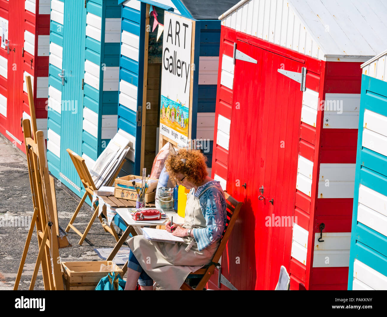 North Berwick, East Lothian, Écosse, Royaume-Uni, 24 juillet 2018. Météo au Royaume-Uni : un artiste au travail dans l'une des cabines de plage colorées s'est transformée en galerie d'art dans la région du port Banque D'Images