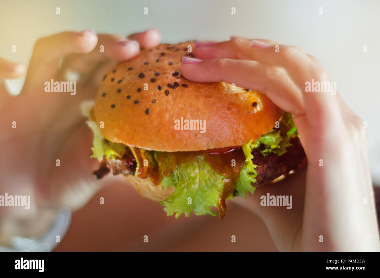 La main avec un délicieux hamburger avec de la laitue et de graines de sésame noir dans un restaurant rustique Banque D'Images