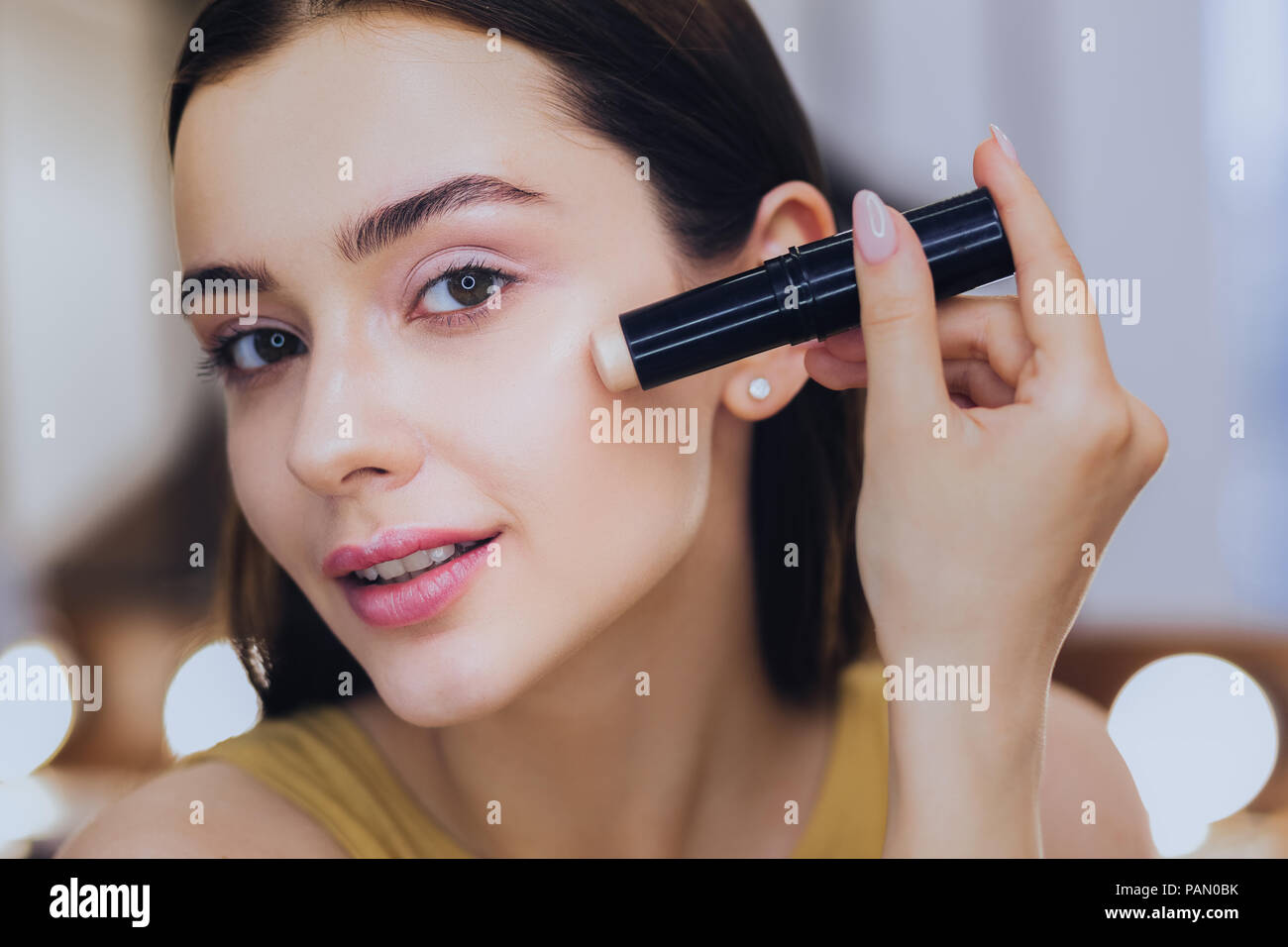 Charmante femme stick correcteur à l'aide tout en mettant sur le maquillage Banque D'Images