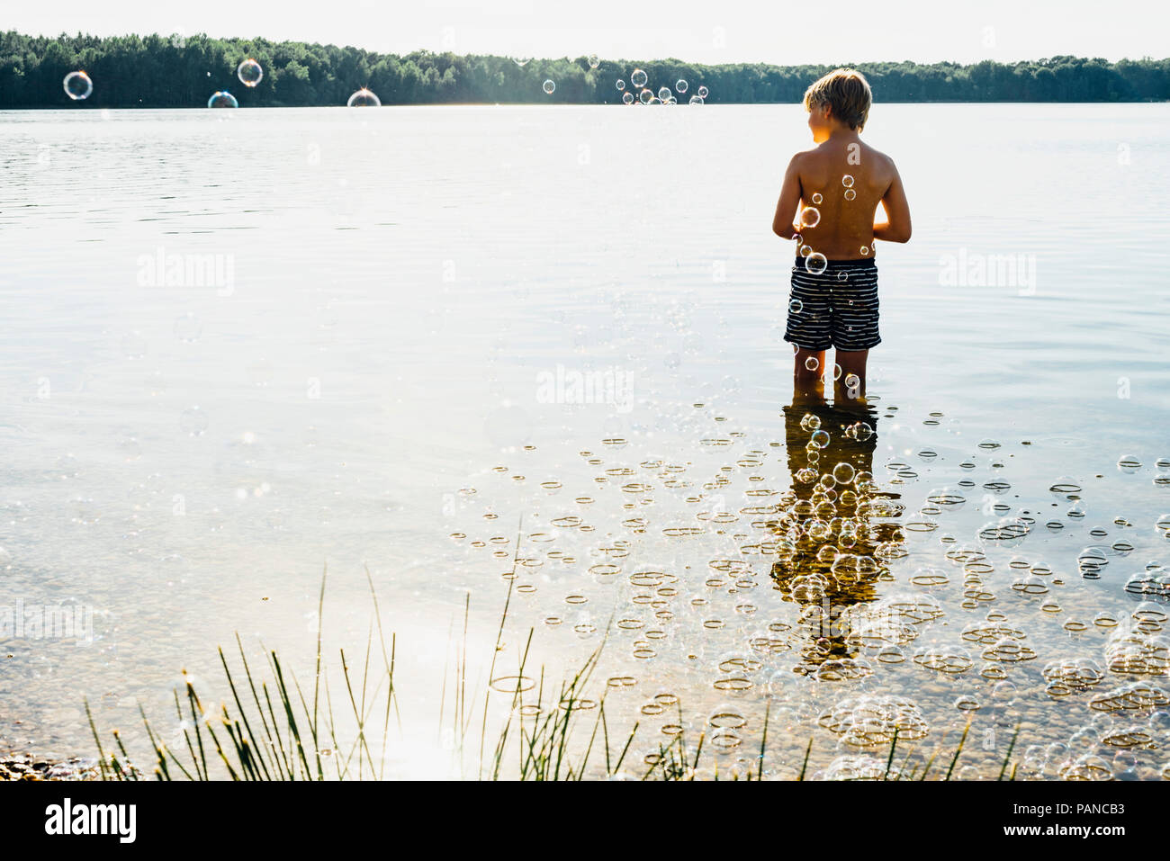 Garçon dans un lac entouré par des bulles de savon Banque D'Images