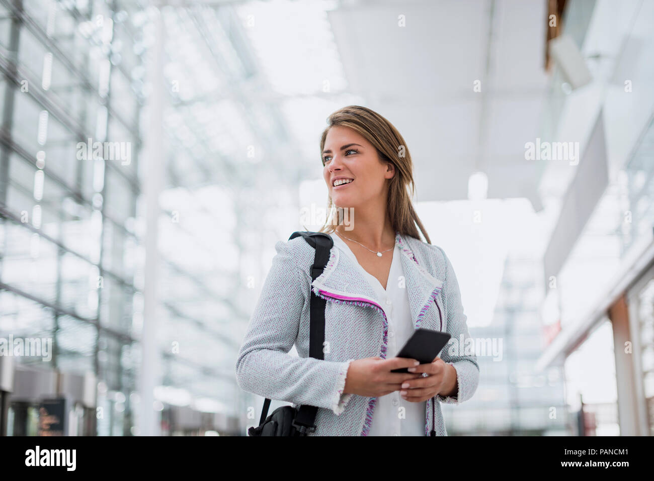 Portrait of smiling young woman with cell phone à l'aéroport à la recherche autour de Banque D'Images