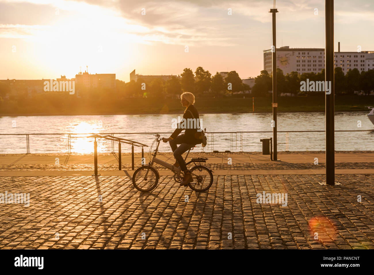 Senior woman riding vélo de ville au bord du fleuve au coucher du soleil Banque D'Images